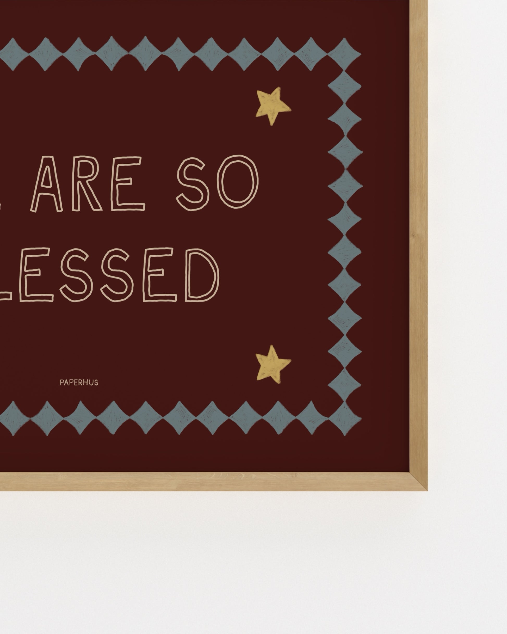 Typography nursery print reading “We Are So Blessed” on a burgundy background with stars and decorative border