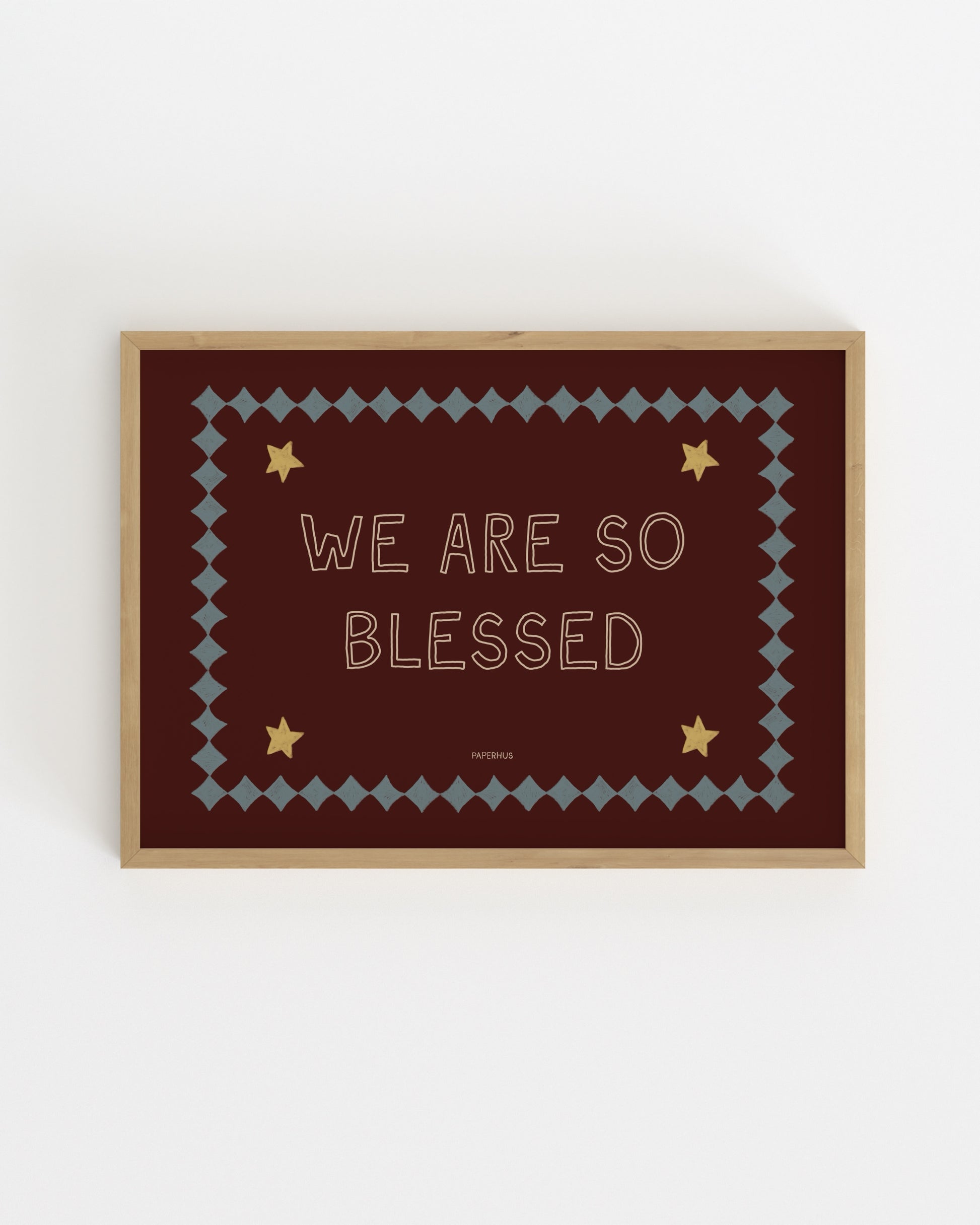 Typography nursery print reading “We Are So Blessed” on a burgundy background with stars and decorative border