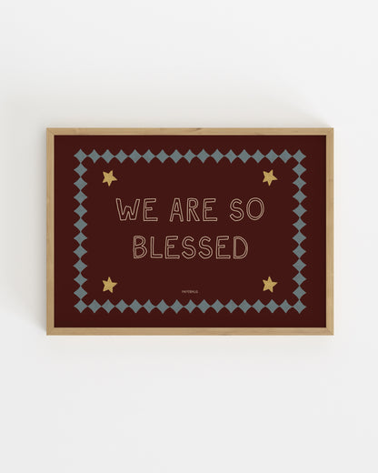 Typography nursery print reading “We Are So Blessed” on a burgundy background with stars and decorative border