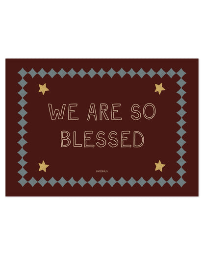 Typography nursery print reading “We Are So Blessed” on a burgundy background with stars and decorative border